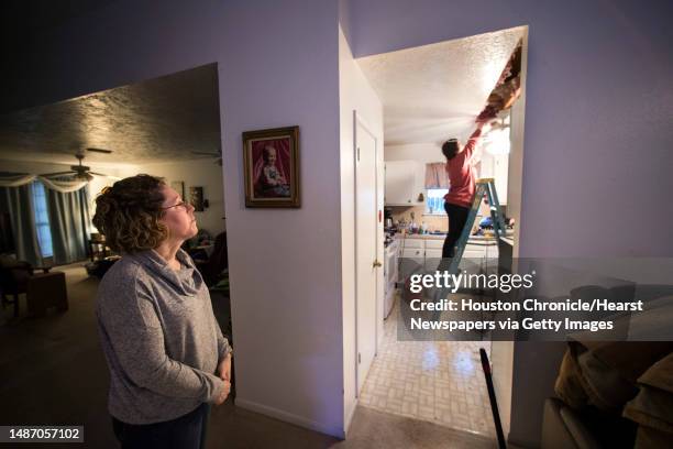 Michelle Toy, left, watches from the living room as Hannah Siqueiros, of HT Innovations, clears insulation from the ceiling after a broken pipe was...