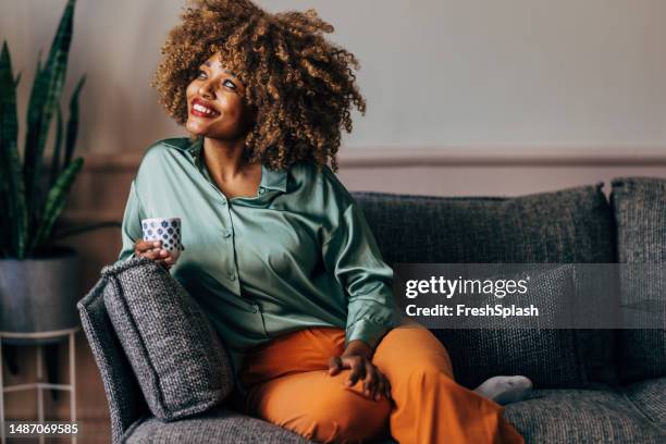 a happy beautiful woman looking away while relaxing at home drinking coffee - coffee happy stock pictures, royalty-free photos & images