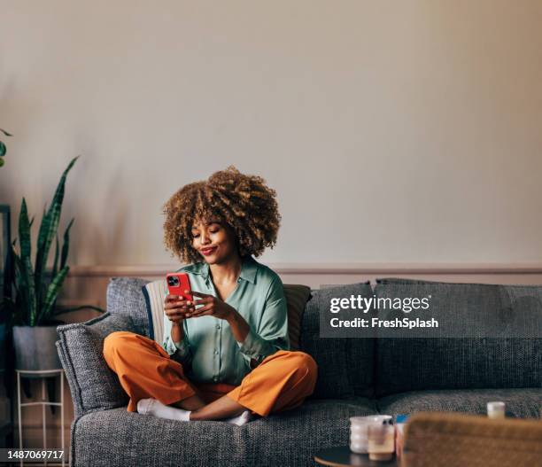 a happy beautiful woman texting on her mobile phone while relaxi - relaxing at home stock pictures, royalty-free photos & images