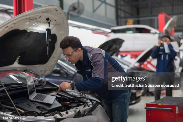 two professional mechanic repairing a car in auto repair garage with digital tablet , computer laptop and doing car service and maintenance. - computerteil stock-fotos und bilder