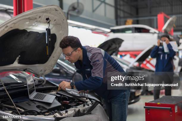 two professional mechanic repairing a car in auto repair garage with digital tablet , computer laptop and  doing car service and maintenance. - chonburi province stock photos et images de collection