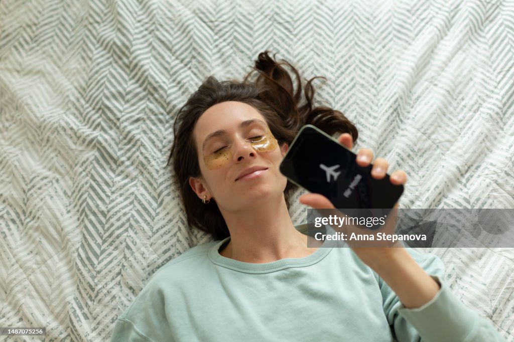 Woman wearing eye patches lying on bed at home