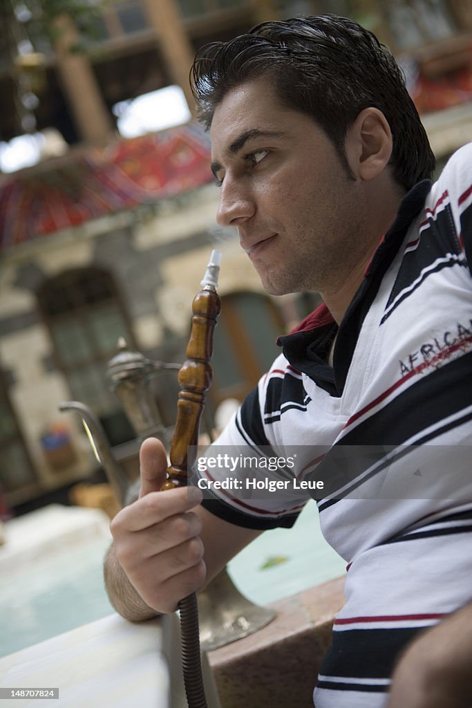 Man smoking sheesha water pipe, Jabri House courtyard restaurant.