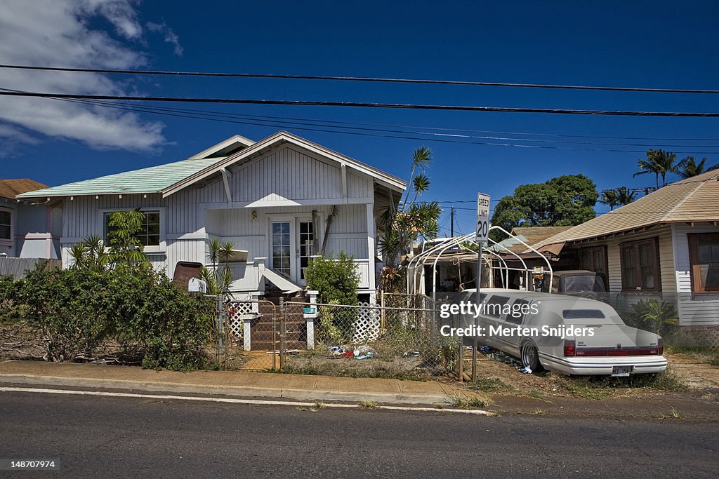 Junk and big limousine in driveway of houses in Wailuku.