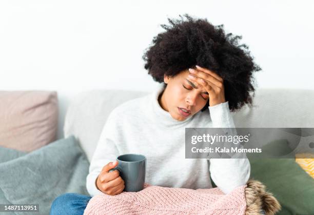 sick african woman sitting on the sofa while holding a mug at home - faiblesse photos et images de collection