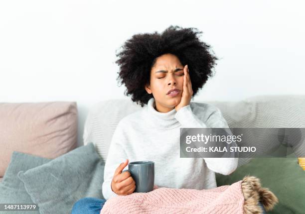 african woman gesturing toothache sitting on the sofa - dor de dentes imagens e fotografias de stock
