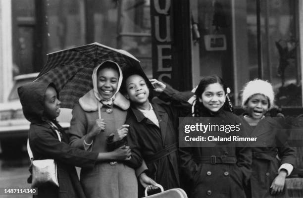 Group of West Indian girls smile in a Notting Hill street and take cover from the rain under an umbrella, London, March 25th 1965.
