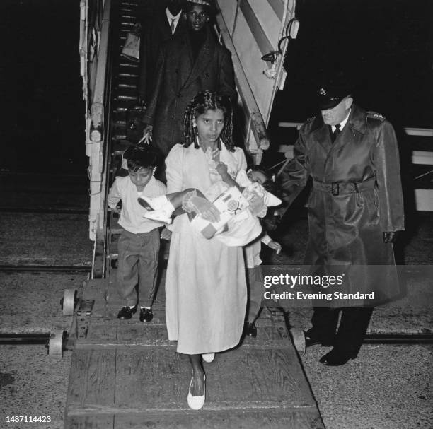 Young mother holding a baby arrives in Britain from a gangplank followed by a young boy and other people from the West Indies, circa 1950.