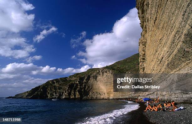 narrow and dwarfed by the cliff behind stretches the well attended pebble beach of pollara, salina island. - beach goers stock pictures, royalty-free photos & images