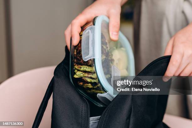 woman puts a lunch box of healthy homemade food, zucchini pancakes and avocado salad in her backpack, healthy lunch to go for school and college students - sack lunch stock pictures, royalty-free photos & images