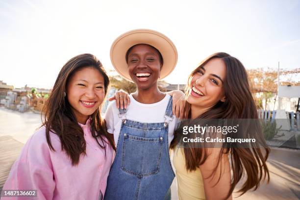 three multirracial young girls embraced looking at camera smiling. - girls flashing camera stock-fotos und bilder