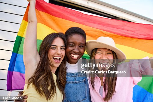 Happy portrait of three girls raising a rainbow flag and looking at camera smiling. Happy portrait of three girls raising a rainbow flag and looking at camera smiling.