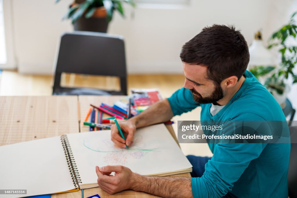 The illustrator man paints some sketches with watercolors at home.