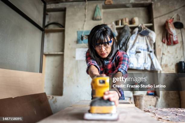 mid adult carpenter using sander while working on a piece of wood at carpentry workshop - elektrisch gereedschap stockfoto's en -beelden