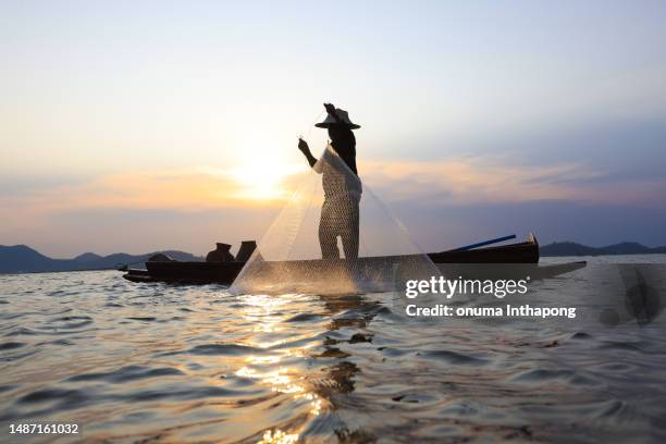 fischer, der sein netz bei sonnenaufgang auswirft. silhouette asiatischer fischer auf holzboot, der ein netz für süßwasserfische auswirft,silhouette fischer fischernetze auf dem boot. thailand - asian fishing boat stock-fotos und bilder