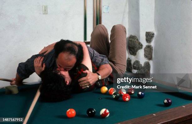 Actor Danny Devito and Actress Rhea Perlman pose for a portrait kissing on their pool table at their home in 1988 in Los Angeles, Ca