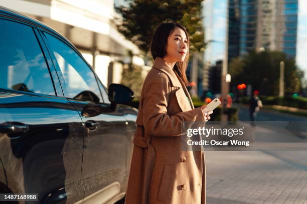 young asian business woman with smartphone standing against the car - free and parking stockfoto's en -beelden