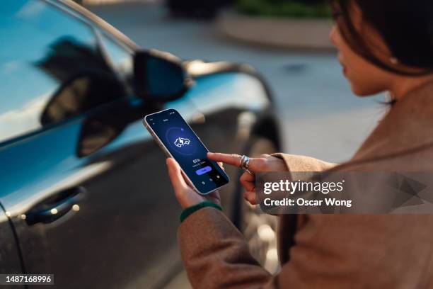 young woman using mobile app on smartphone to manage charging electric car - coche eléctrico coche de combustible alternativo fotografías e imágenes de stock