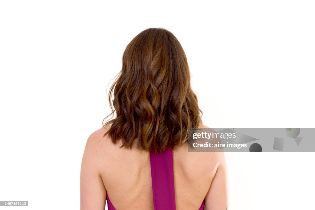 Rear view of a beautiful woman standing with a purple dress and long hair with white background.