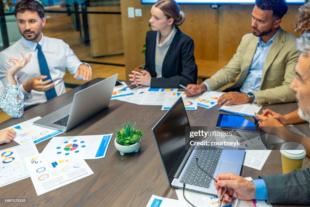 . The documents on the conference table have financial or marketing figures, graphs and charts on them.