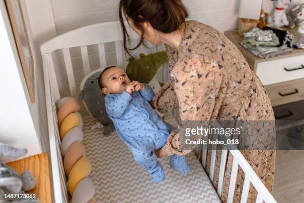 young mother putting her cute baby boy to sleep in baby crib - modern baby nursery stock pictures, royalty-free photos & images