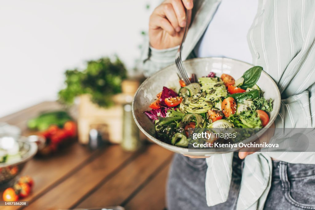 Woman mixing delicious superfood salad ingredients with wooden spoons in kitchen