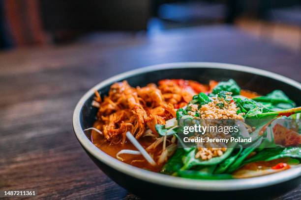 close-up shot of korean spicy kimchi ramen in a bowl with bok choy and nuts - korean food stock pictures, royalty-free photos & images