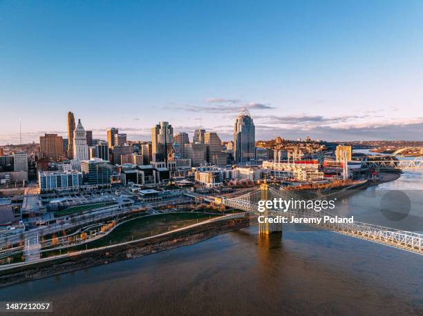 high angle view at sunset of the john a. roebling suspension bridge with downtown cincinnati along the ohio river - cincinnati business stock pictures, royalty-free photos & images