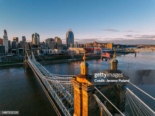 high angle view of the bennington 76 flag and commonwealth of kentucky flag flying on the john a. roebling bridge with downtown cincinnati along the ohio river - cincinnati business stock pictures, royalty-free photos & images