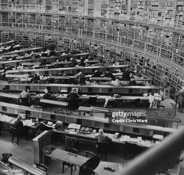 High-angle view showing people sitting at tables, with the walls lined with shelves of books, in the Reading Room in the Great Court of the British...