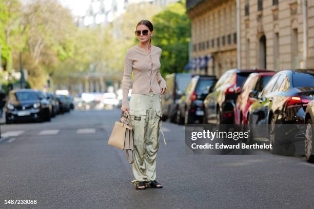 Diane Batoukina wears dark brown squared large sunglasses from Dior, a beige ribbed wool / buttoned cardigan from Fendi, pale green silk / satin...