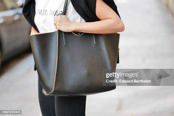 Diane Batoukina wears a white with black faded logo print pattern t-shirt from Saint Laurent Paris, a black wool pullover knot at the shoulder, a...