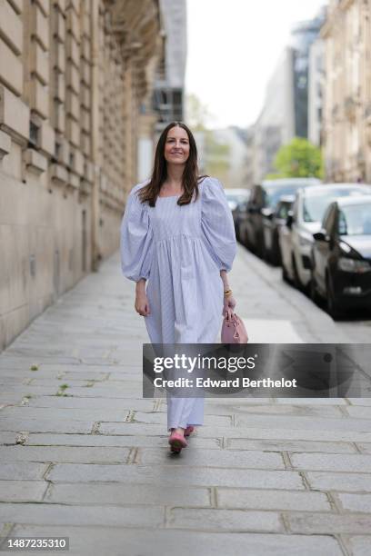 Alba Garavito Torre wears gold and green embossed pattern earrings, a baby blue and white striped print pattern puffy short sleeves / long dress from...
