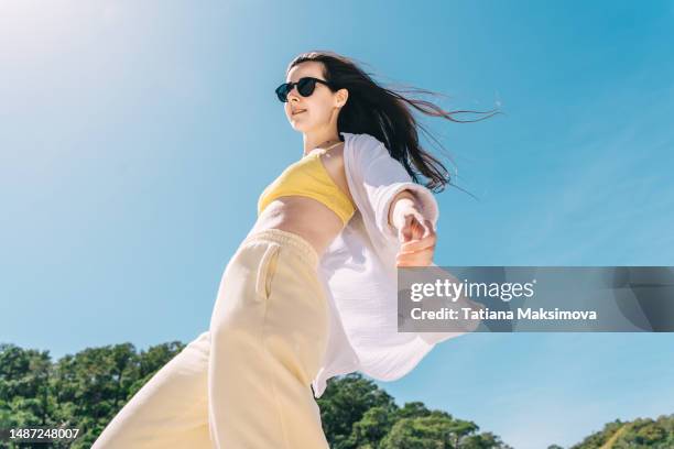 beautiful young woman in sunglasses and white muslin shirt have a fun on the beach, blue sky on background. bottom view. - óculos escuros acessório ocular - fotografias e filmes do acervo