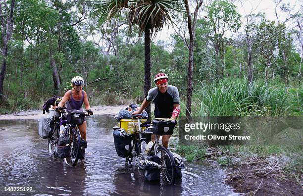 a pair of touring cyclists pushing their bikes through water as they approach bamaga, having riden from melbourne in the far south. - riden stock pictures, royalty-free photos & images