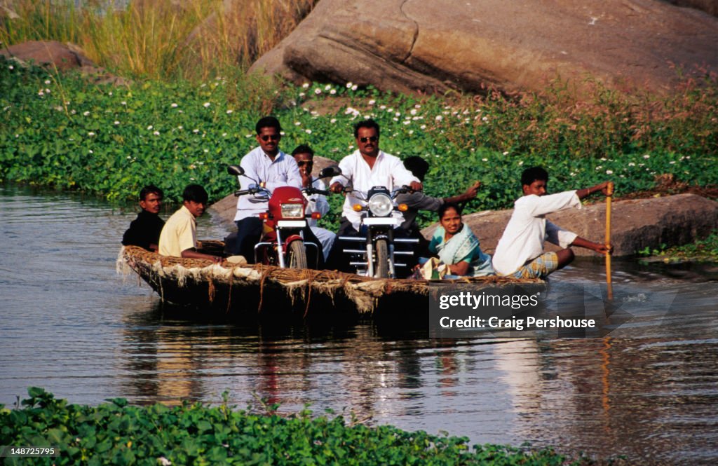 Man paddling passengers and motorbikes in coracle (basket boat) on Tungabhadra River.