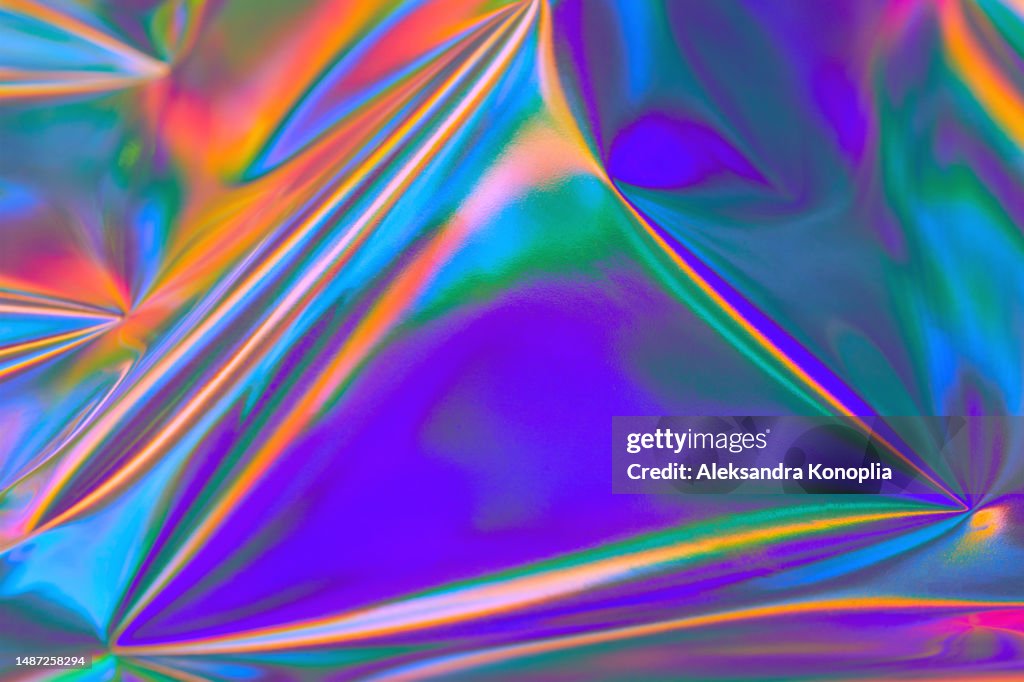 Abstract vibrant purple, blue, mint green, orange, red metallic psychedelic holographic wrinkled foil texture. Bold bright neon colored crazy new wave groovy style background