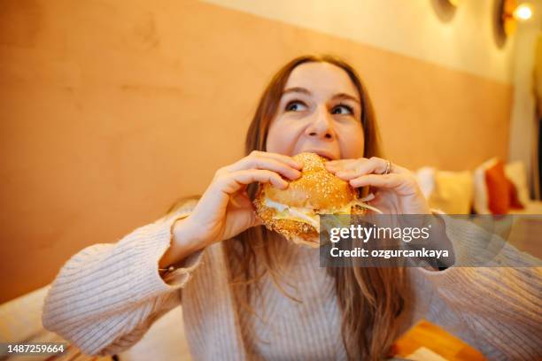 woman eating a hamburger in modern fastfood cafe, lunch concept - morder imagens e fotografias de stock