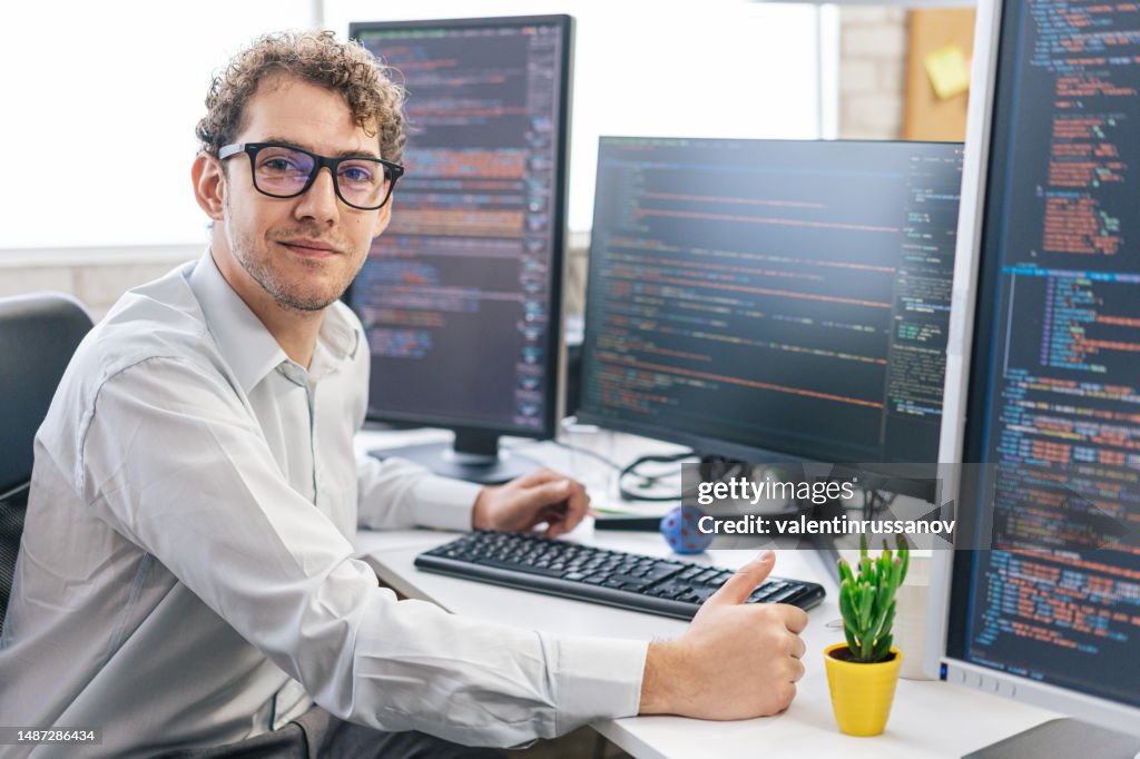 Porträt einer jungen lächelnden Programmiererin, die mit Computern in einem IT-Büro auf ihrem Schreibtisch sitzt