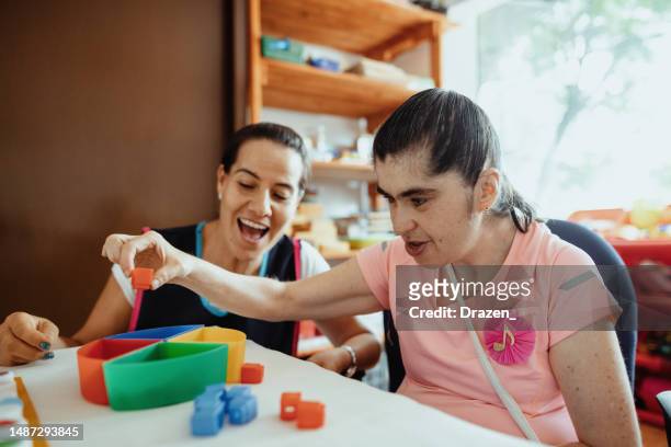 mature teacher working in nursery with person with down syndrome - learning disability nurse stock pictures, royalty-free photos & images