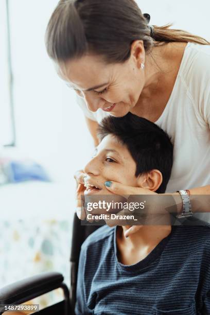 teenager boy with celebral palsy at home in wheelchair, massaged by mother - needs improvement stock pictures, royalty-free photos & images