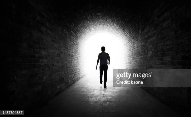 joven caminando por un túnel oscuro - luz al final del túnel fotografías e imágenes de stock