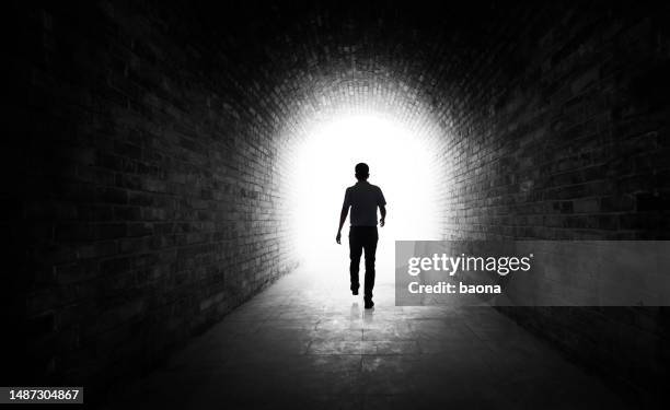 giovane che cammina attraverso un tunnel buio - luce alla fine del tunnel foto e immagini stock
