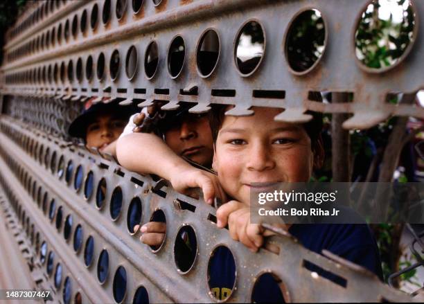 Children on Mexico side, peer through a gap in the metal barrier at Calexico Border crossing, December 23, 1986 in Calexico, California.