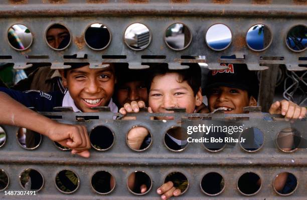 Children on Mexico side, peer through a gap in the metal barrier at Calexico Border crossing, December 23, 1986 in Calexico, California.