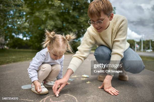 mother and daughter drawing face with chalk on asphalt - family chalk drawing stock pictures, royalty-free photos & images