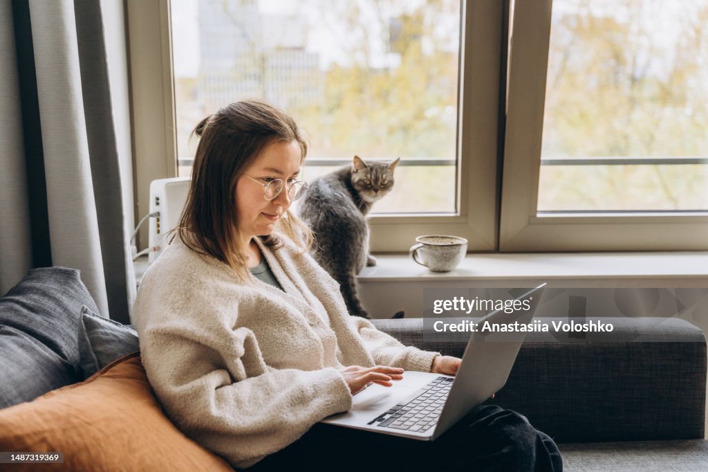 Young woman working at home remotely using a laptop while sitting on the sofa