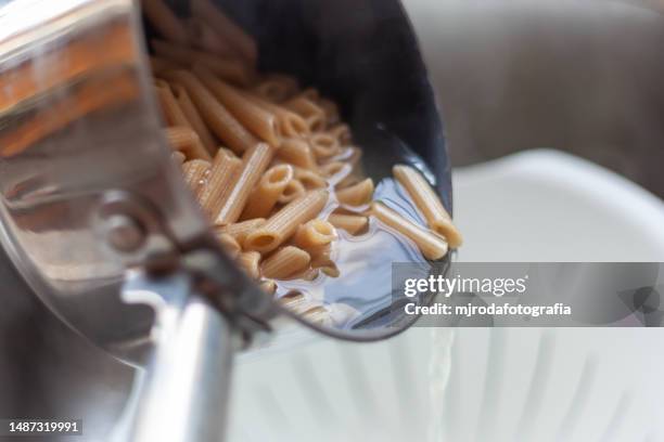 whole grain macaroni. pouring the cooked macaroni from the pot into the colander - colander foto e immagini stock