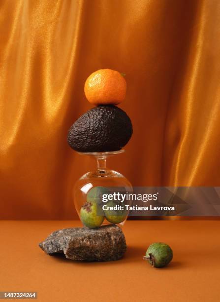 conceptual seasonal still life. abstract composition made of stones, glass, avocado and fruit. natural products layout on golden orange background. - still life stock pictures, royalty-free photos & images