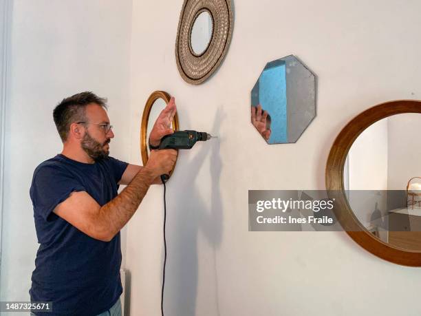 man drilling the wall with a drill to hang a mirror - drill bit stock pictures, royalty-free photos & images